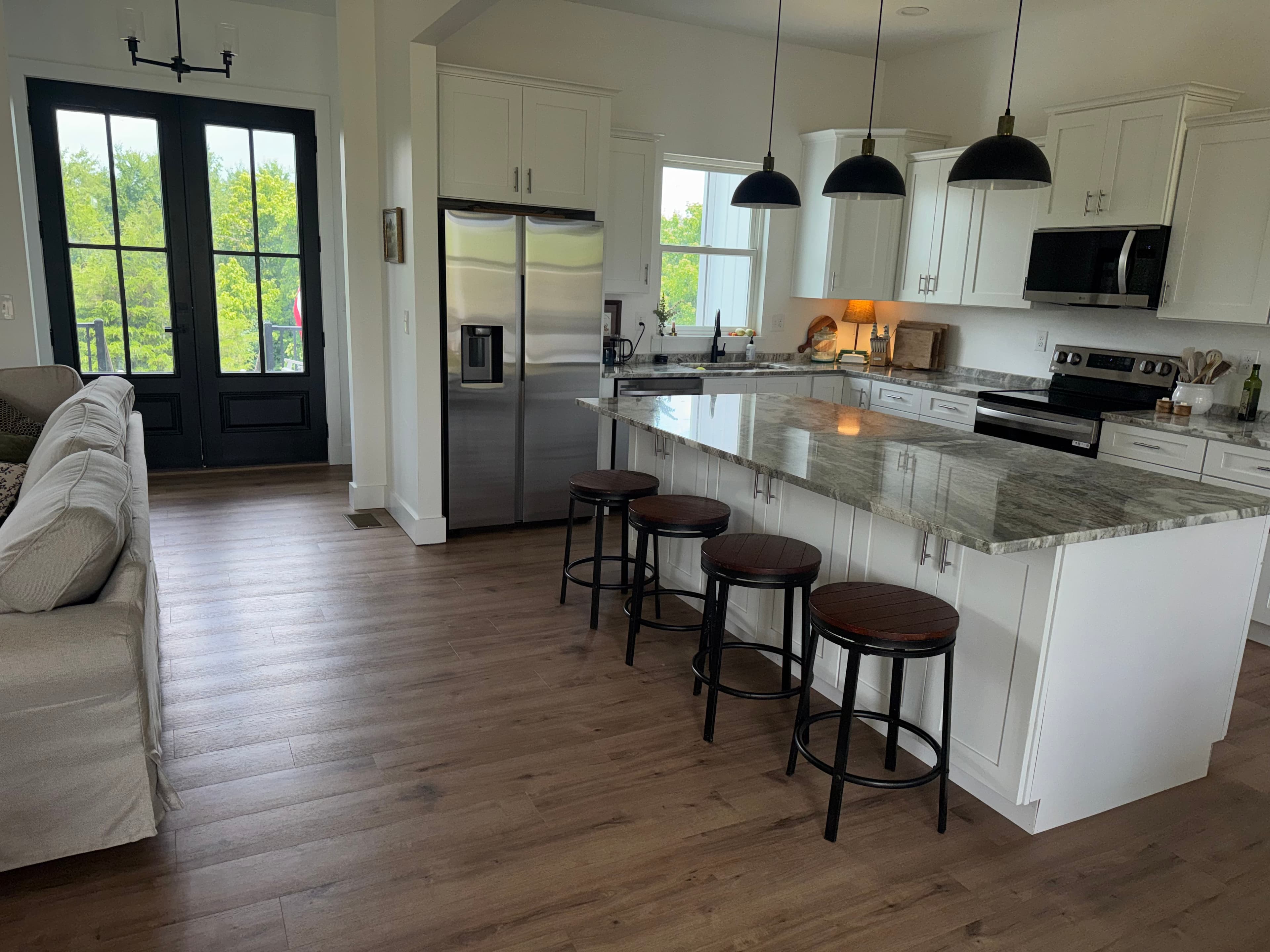Modern white kitchen featuring a marble island, four bar stools, and black pendant lights.