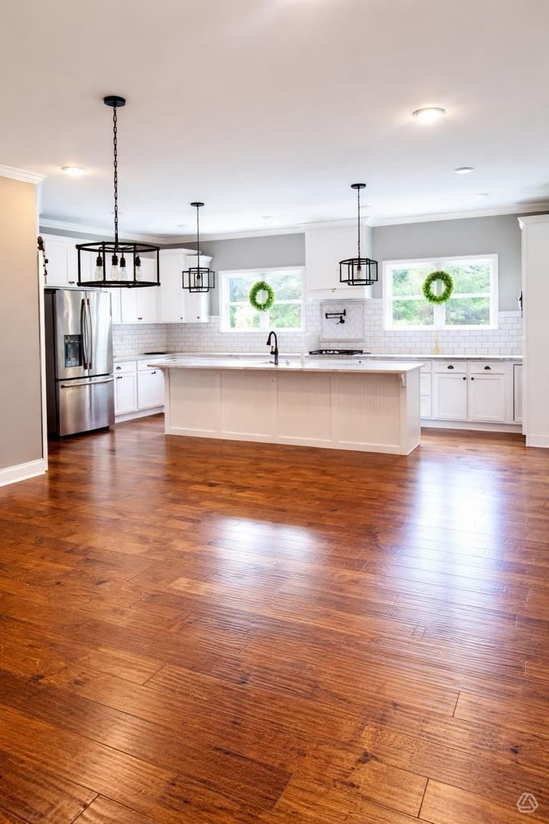 Modern white kitchen featuring a large island, dark wood floors, and black industrial pendant lights.